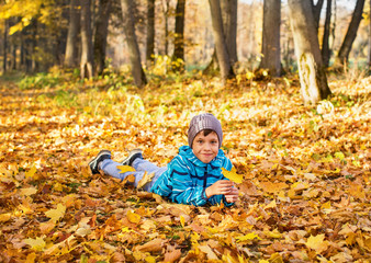 Child boy in autumn park with foliage. He lies on the yellow leaves.