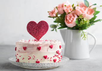 Close Up of a cake decorated with small hearts with heart cake topper, against a gray background....