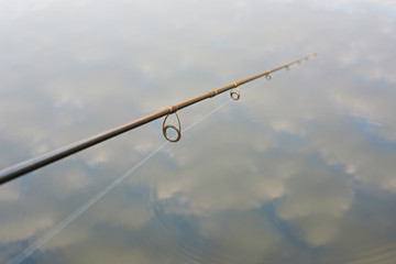 fishing rod on background of water with reflected clouds