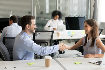 Smiling male and female colleagues shaking hands in shared office thanking for successful work, happy employees handshaking satisfied with good result and help in collaboration teamwork concept