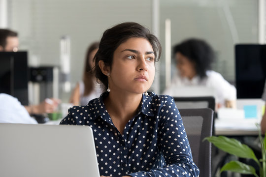 Thoughtful indian business woman looking away feeling bored pensive thinking of problem solution in office with laptop, serious hindu employee searching new ideas at work unmotivated about dull job
