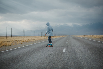 Obraz premium Young sporty girl with longboard is standing on a deserted road