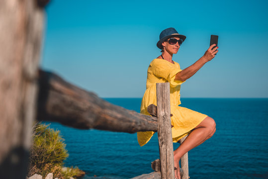 Woman sitting on a wooden fence by the sea and taking selfie
