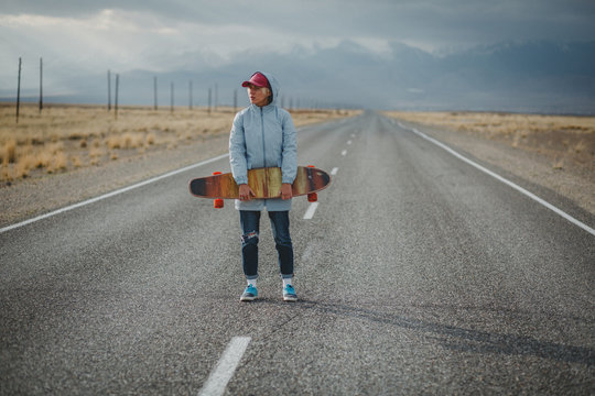 Young sporty girl with longboard is standing on a deserted road
