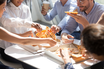 Diverse business office people group taking sharing pizza slices from box on table, staff employees team workers eating together enjoy lunch at work break, delivery service concept, close up view