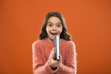 Childrens literature. Girl hold book read story over orange background. Child enjoy reading book....