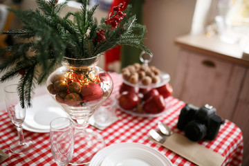 New Year's home interior. Garlands in bokeh. Beautiful red and white plates and cups on a wooden table. Cozy atmosphere. Christmas mood with camera.