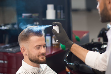 Barber fixating hair of male with spray in barber shop
