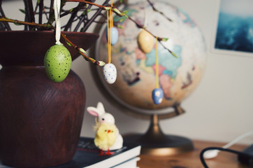 Small Easter eggs hanging from the ament branches with a chich, bunny and a globe in the background.