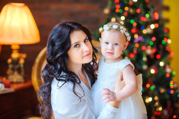 beautiful mother playing with her little daughter sitting in a chair near the festive Christmas tree