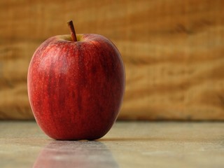Close-up of a fresh red apple over a marble surface, against a wooden background. Healthy and yummy fruit. There is room for text.