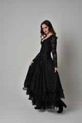 Fototapeta premium full length portrait of brunette girl wearing long black gown with corset. standing pose on grey studio background.