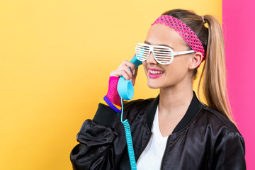 Woman in 1980's fashion with old fashioned phone on a split yellow and pink background