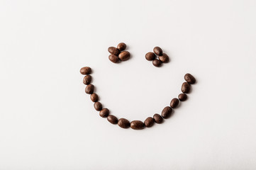 Fair trade roasted organic coffee beans arranged as a smile on white background - Concept of caffeine addiction, breakfast, energy or morning happiness - Coffee shop, cafe and restaurant decor