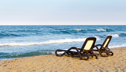 Fototapeta na wymiar Lonely pair of beach deckchairs on seashore in front of sea, sunset.