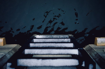 A snowy ladder descending into a cold deep water.