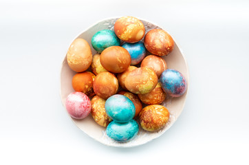 Flat lay traditional colourful dyed easter eggs in a ceramic bowl in a white background.
