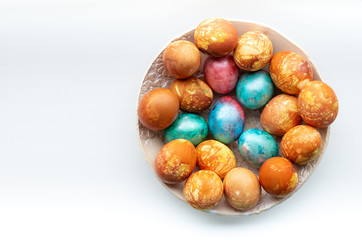 Flat lay traditional colourful dyed easter eggs in a ceramic bowl in a white background.