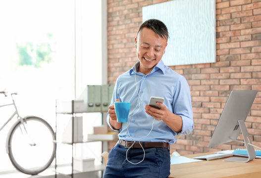 Happy young businessman with mobile phone listening to music in office. Peaceful moment