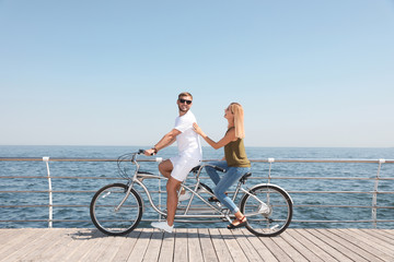 Couple riding tandem bike near sea on sunny day