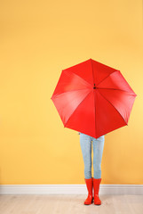 Woman hiding behind red umbrella near color wall