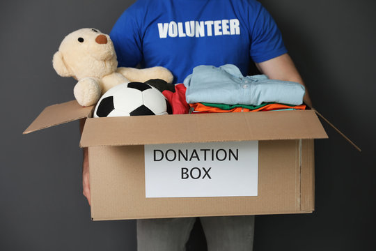 Male volunteer holding box with donations on grey background