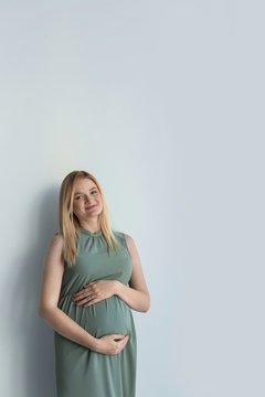 Young pregnant woman touching belly on light background
