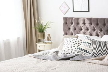 Comfortable bed with cushions in stylish bedroom interior