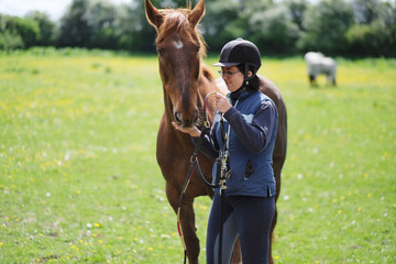 Woman rider in special outfit gives food from the horse's hand to the pasture