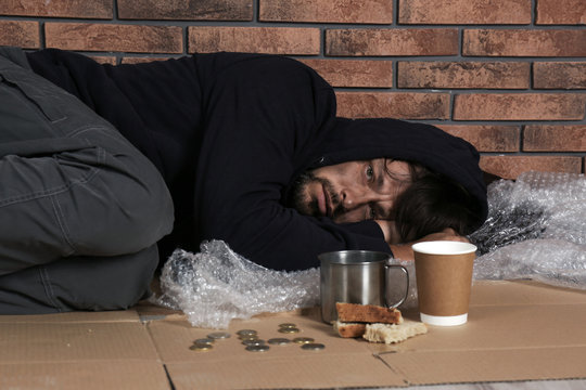 Poor homeless man lying on floor near brick wall