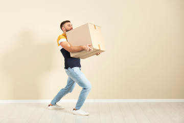 Full length portrait of young man carrying carton box near color wall. Posture concept