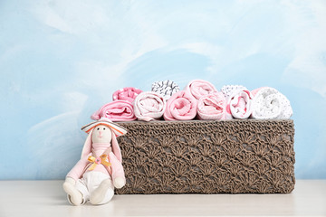 Basket with baby clothes and toy on table near color wall