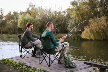 Friends fishing on wooden pier at riverside. Recreational activity