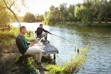 Keuken foto achterwand Vissen Friends fishing on wooden pier at riverside. Recreational activity