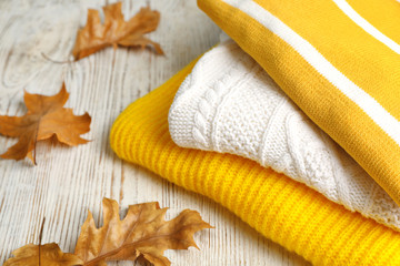 Stack of folded knitted sweaters and autumn leaves on table. Space for text