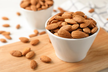 Tasty organic almond nuts in bowl on wooden board. Space for text