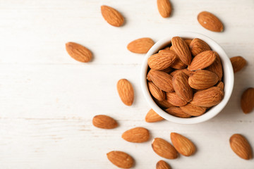 Tasty organic almond nuts in bowl and space for text on table, top view