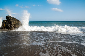 Sea waves breaking against a big rock on the foreshore at the beach