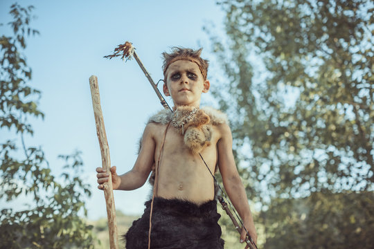 Caveman, manly boy with staff and bow hunting near river. Prehistoric tribal boy outdoors on nature. Young shaggy and dirty savage, warrior and hunter with weapon. Primitive ice age man in animal skin
