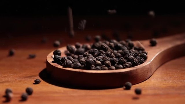 Black Tellicherry peppercorns closeup in wooden spoon on a kitchen table.