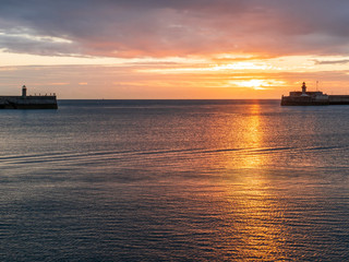 Fototapeta na wymiar Beautiful orange sunrise reflections in the ocean at Dun Laoghaire harbor in Dublin, Ireland