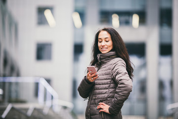 Business lady. Beautiful caucasian brunette woman uses technology mobile phone pink against background of the plastic facade of the window. The girl is calling, talking on the phone. Theme Business