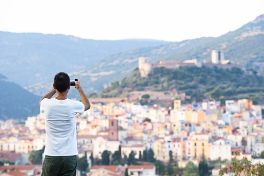 A tourist is taking a picture with his phone at the beautiful and colorful village of Bosa  located in the north-west of Sardinia, Italy.