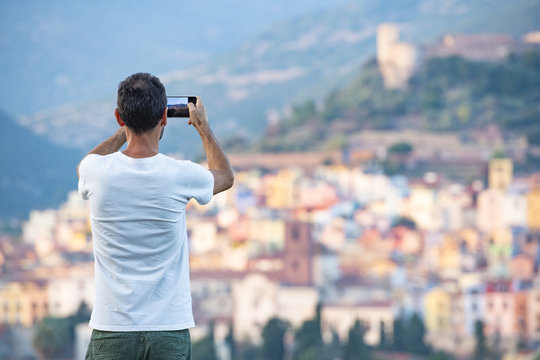 A tourist is taking a picture with his phone at the beautiful and colorful village of Bosa  located in the north-west of Sardinia, Italy.