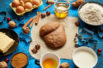 Ready for next step raw gingerbread dough placed among various ingredients. Christmas baking concept. Placed on blue background. View from above.