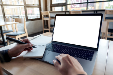 Mockup image of hands using laptop with blank white desktop screen while writing on a notebook in office