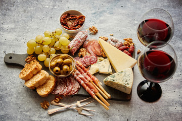 Antipasto platter cold meat and cheese board with grapes, wine, various kinds of cheese, grissini bread sticks on white rustic background. View from above