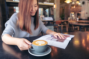 Closeup image of a beautiful asian woman reading magazine while drinking coffee in modern cafe