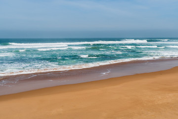 Fototapeta na wymiar Summer day and sandy beach background. Golden sand and soft blue ocean waves on Guincho Beach (Praia da Guincho) in Cascais, Portugal. 