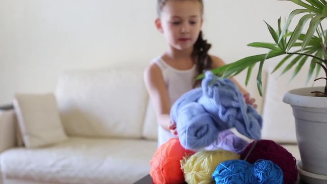 A girl with a mobile phone on the couch. On the table there are threads for knitting in different colors.